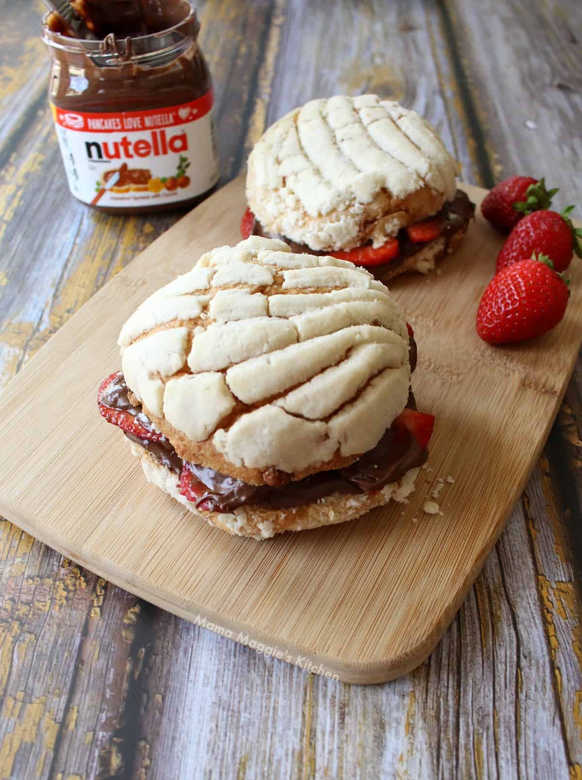 A picture of nutella stuffed conchas on a wooden cutting board next to an open container of nutella.