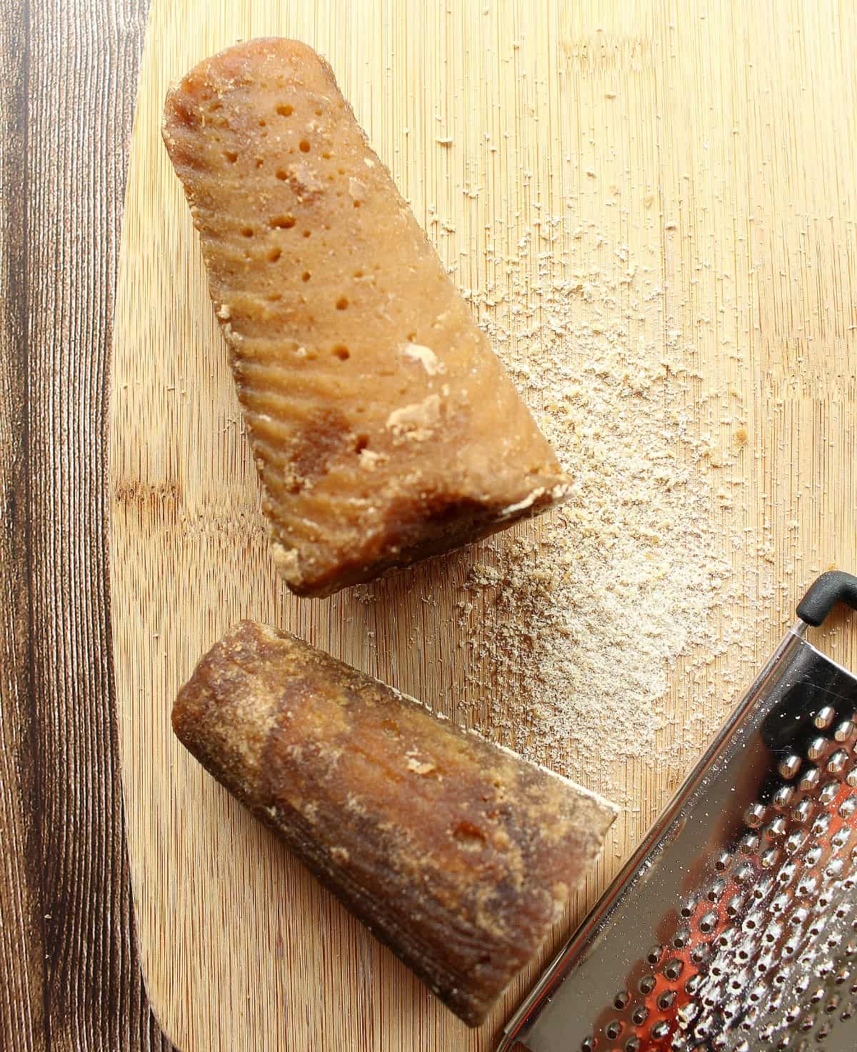 Two piloncillo cones next to grated sugar and a metal grater.