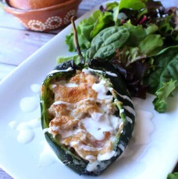 A pork chile relleno on a white plate drizzled with crema mexicana and next to a bed of lettuce.