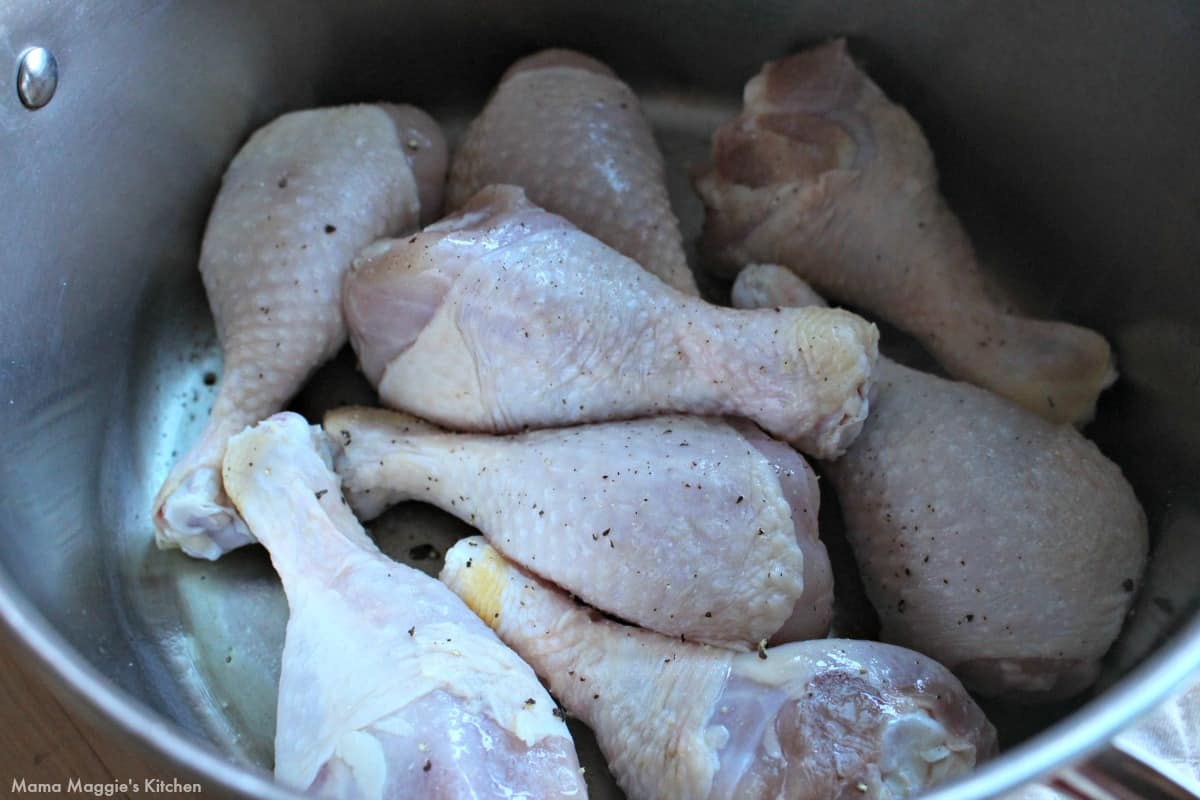 Raw chicken legs cooking in a large stock pot.
