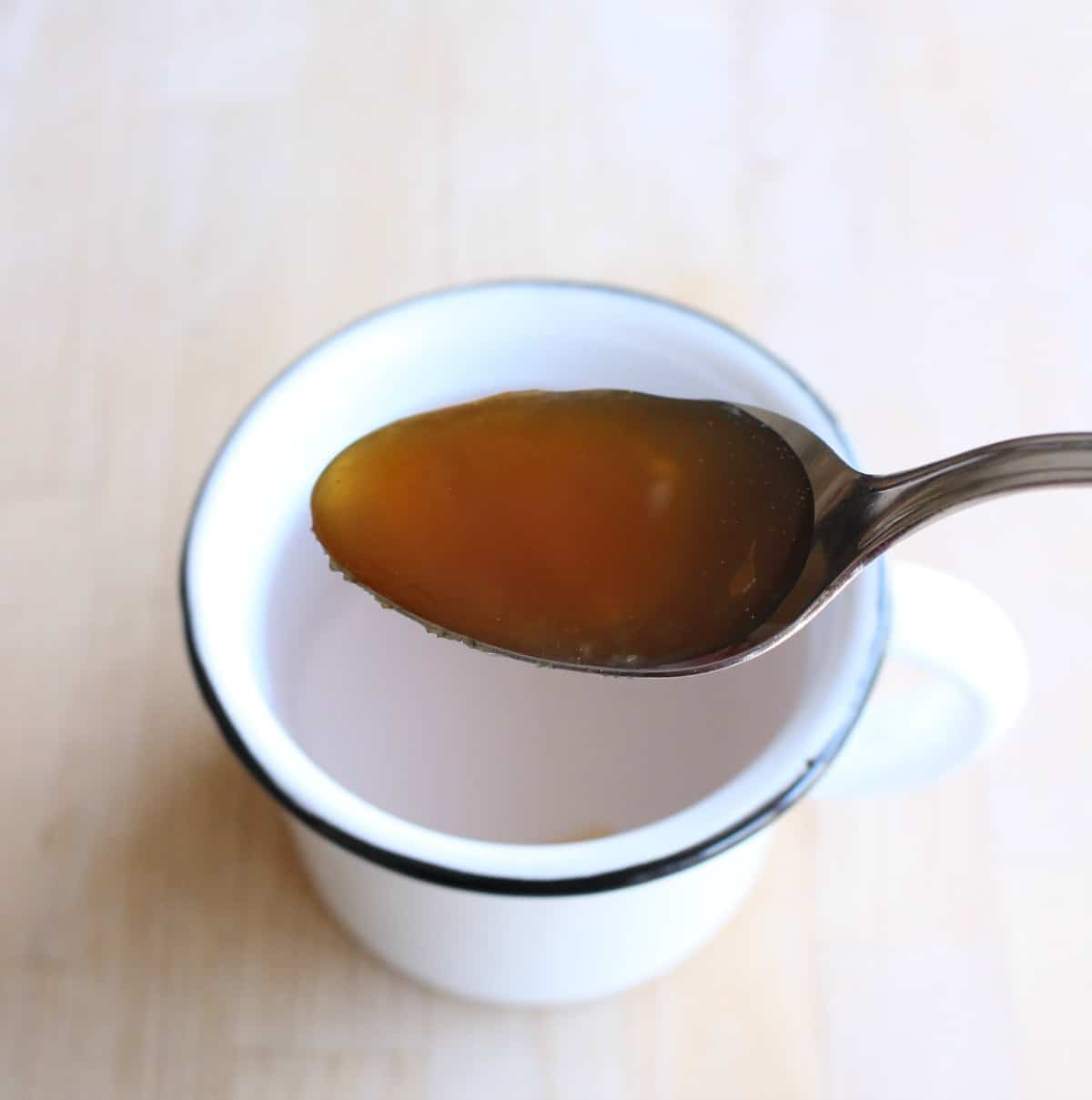 A spoon with honey over a white cup.