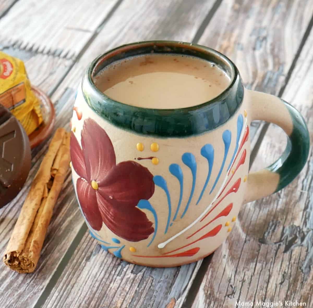 Atole de Chocolate served in a decorative Mexican cup next to a cinnamon stick.