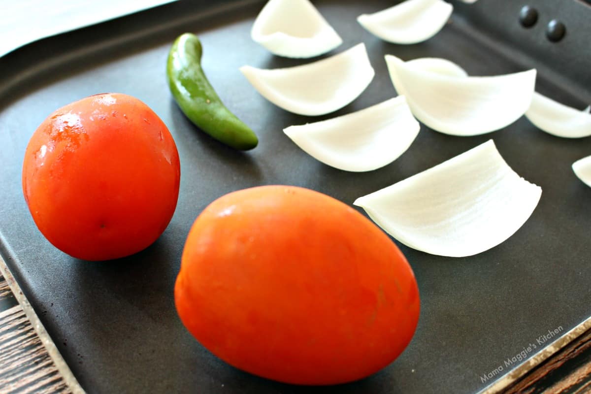 Tomatoes, serrano, onion, and garlic roasting on a skillet.