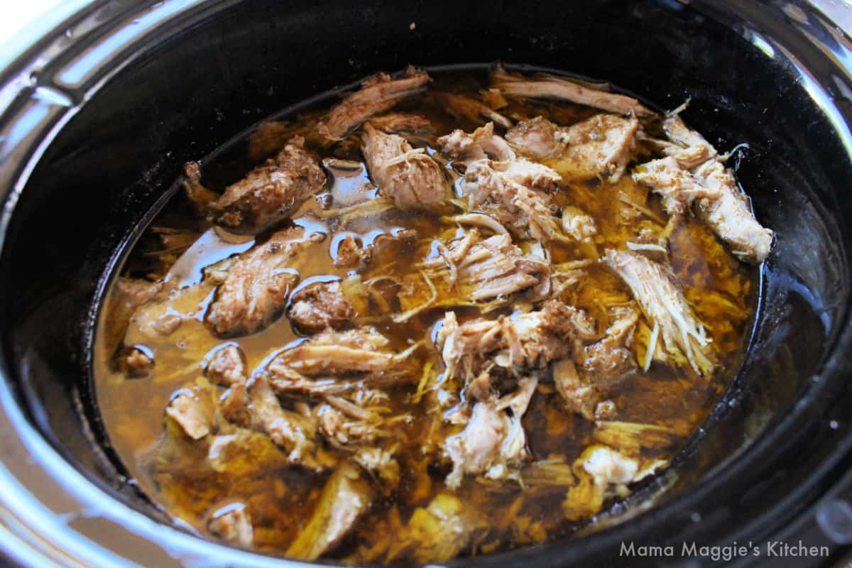 Shredded Ancho Pork in a slow cooker with its juices.
