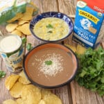 Crema de Frijol Negro and Caldo de Queso served in bowls and surrounded by chips and other ingredients.