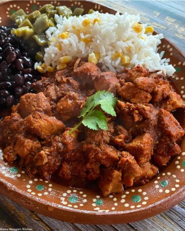 Asado de Puerco served on a decorative clay plate next to rice, beans, and nopales.