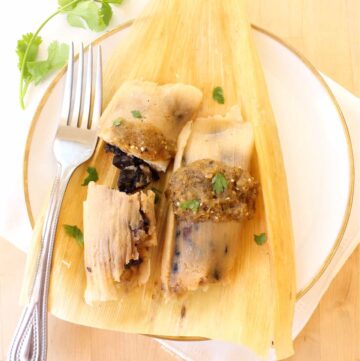 Two tamales on a corn husk topped with salsa, cilantro, and served with a fork.