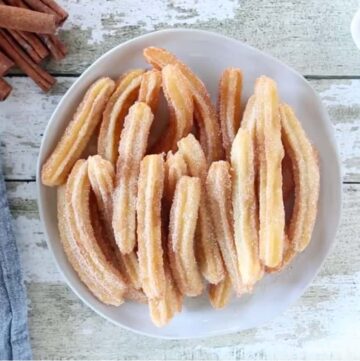 A pile of churros served on a white bowl.