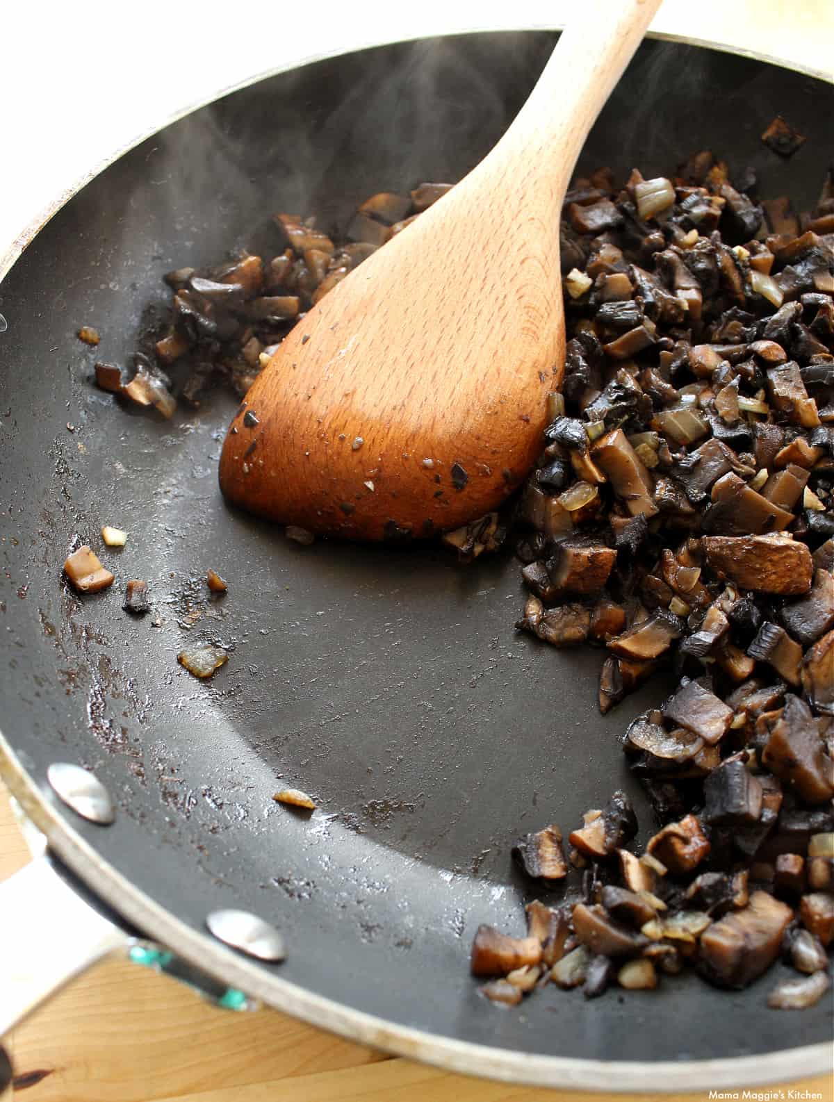 A wooden spoon cooking mushrooms in a skillet.