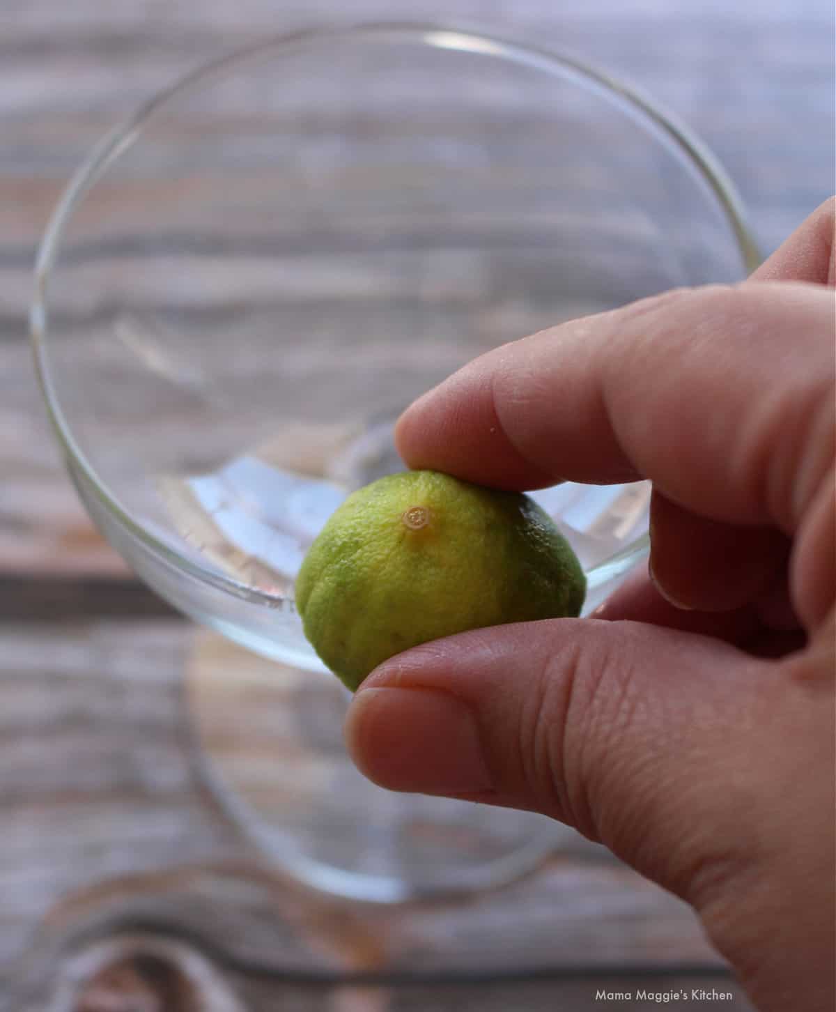 A hand holding a cut lime and rubbing it over the edge of a glass rim.