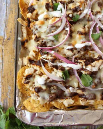 A sheet pan with Chicken Mole Nachos topped with red onion slices.
