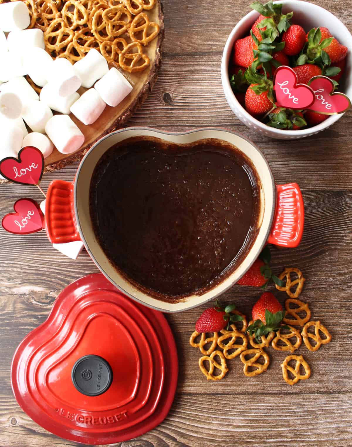 A heart-shaped pot with Mexican chocolate fondue and surrounded by dipping ingredients.