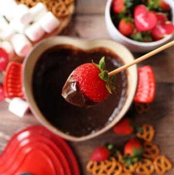 A skewer holding a strawberry covered in chocolate over the fondue pot.