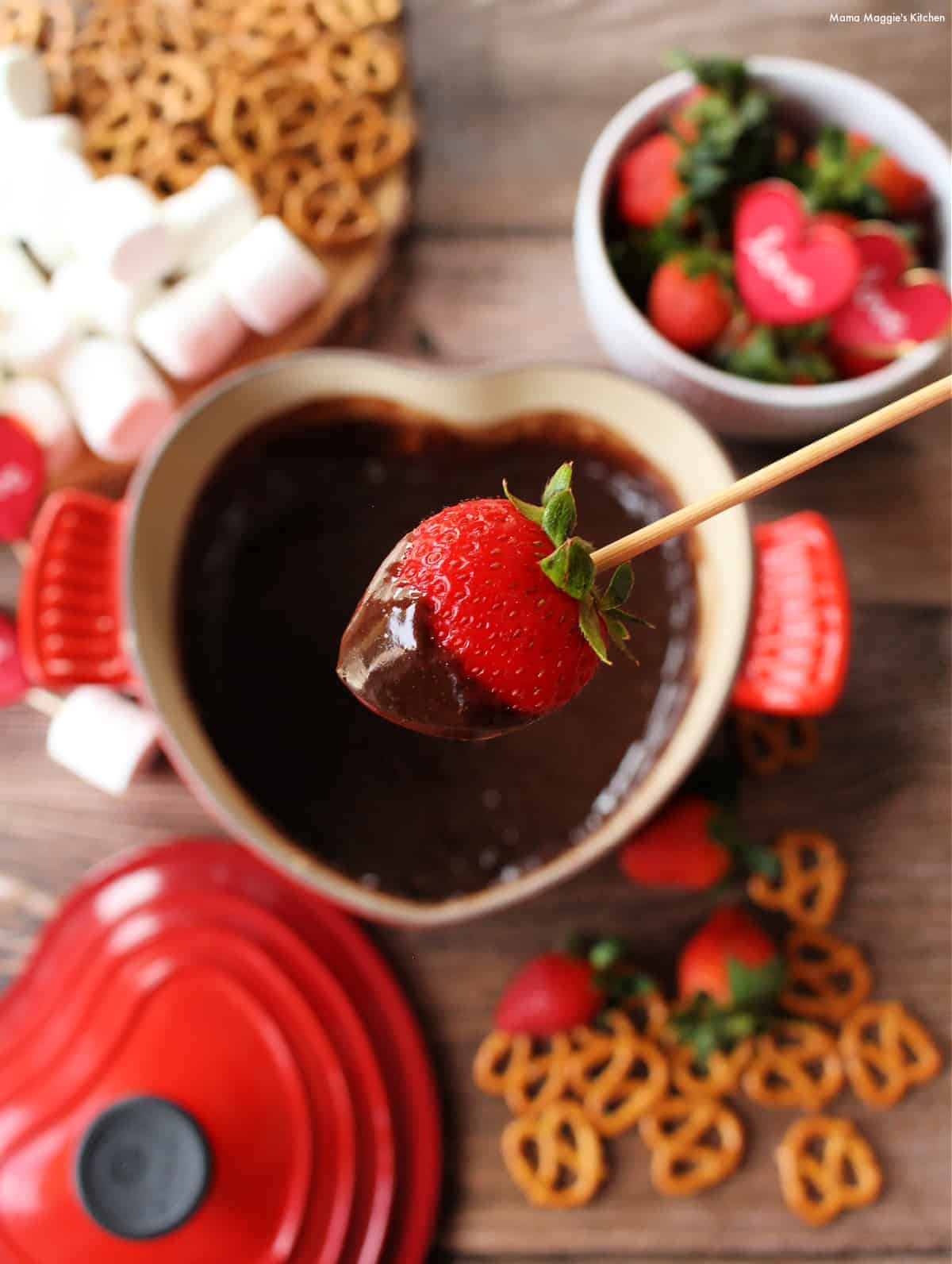 A skewer holding a strawberry covered in chocolate over the fondue pot.