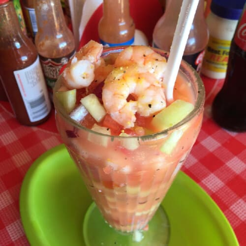 A coctel de camaron served in a glass cup with a plastic white spoon.