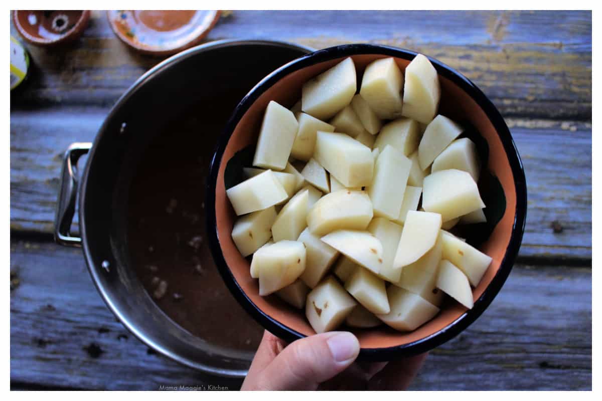 A hand holding a bowl of raw potatoes over the stock pot.