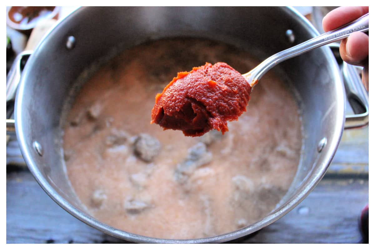 A spoon holding tomato paste over a stock pot.