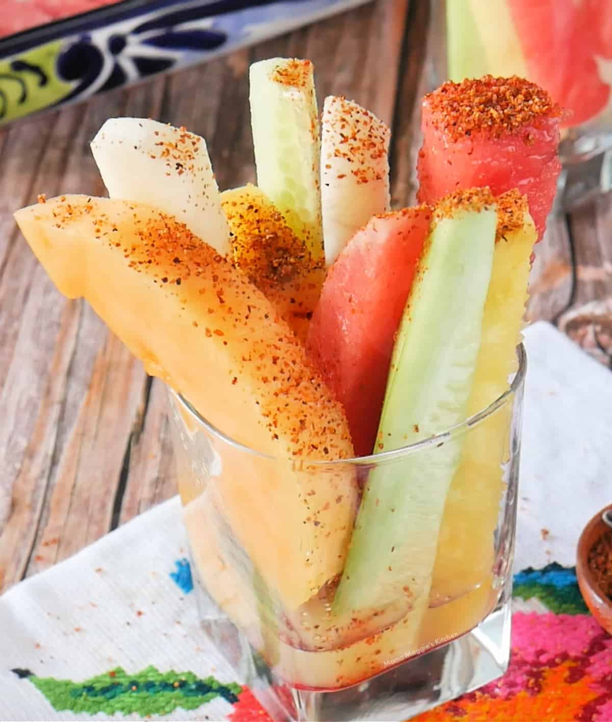 A glass cup full of fruit and sprinkled with Tajin.