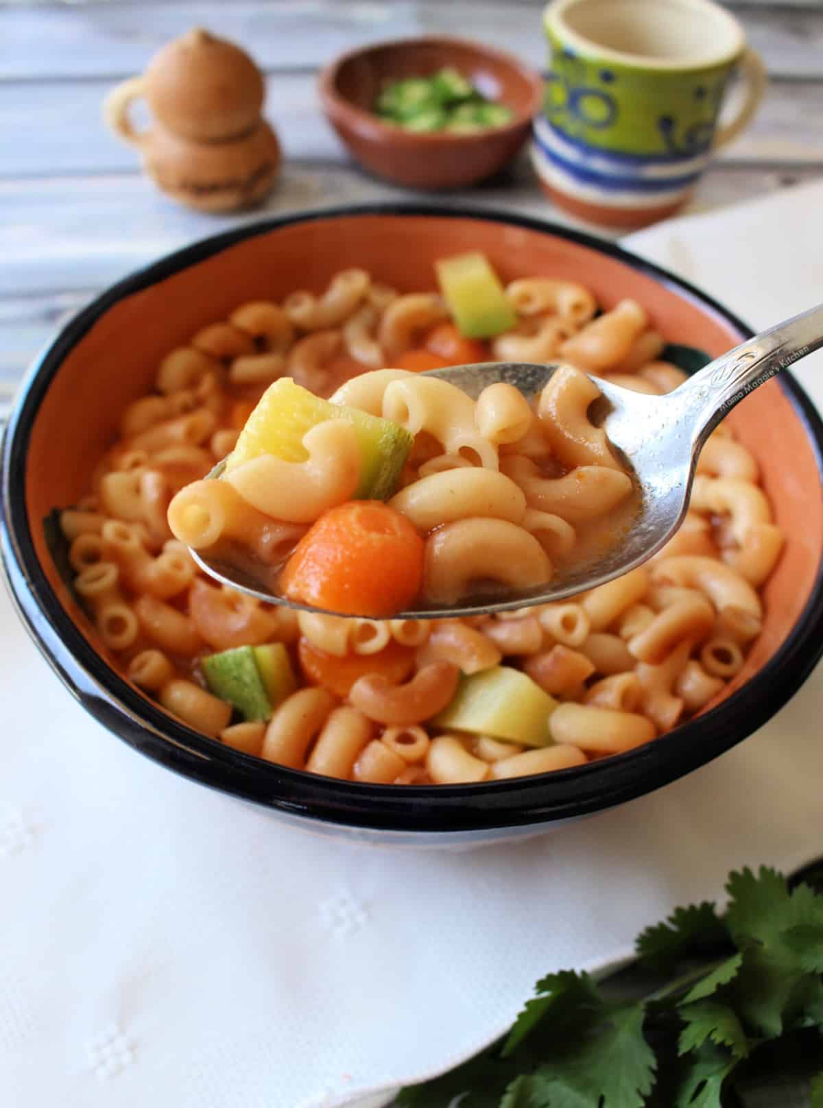 A spoon holding sopa de coditos over a bowl.