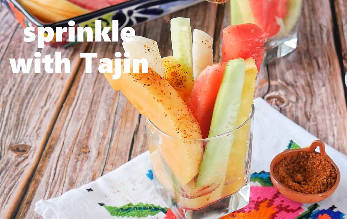 A glass cup full of fruit and sprinkled with Tajin.