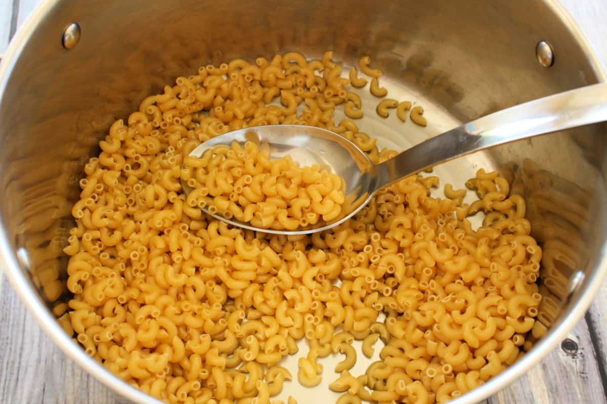 A pot with a cooking spoon toasting the elbow macaroni.