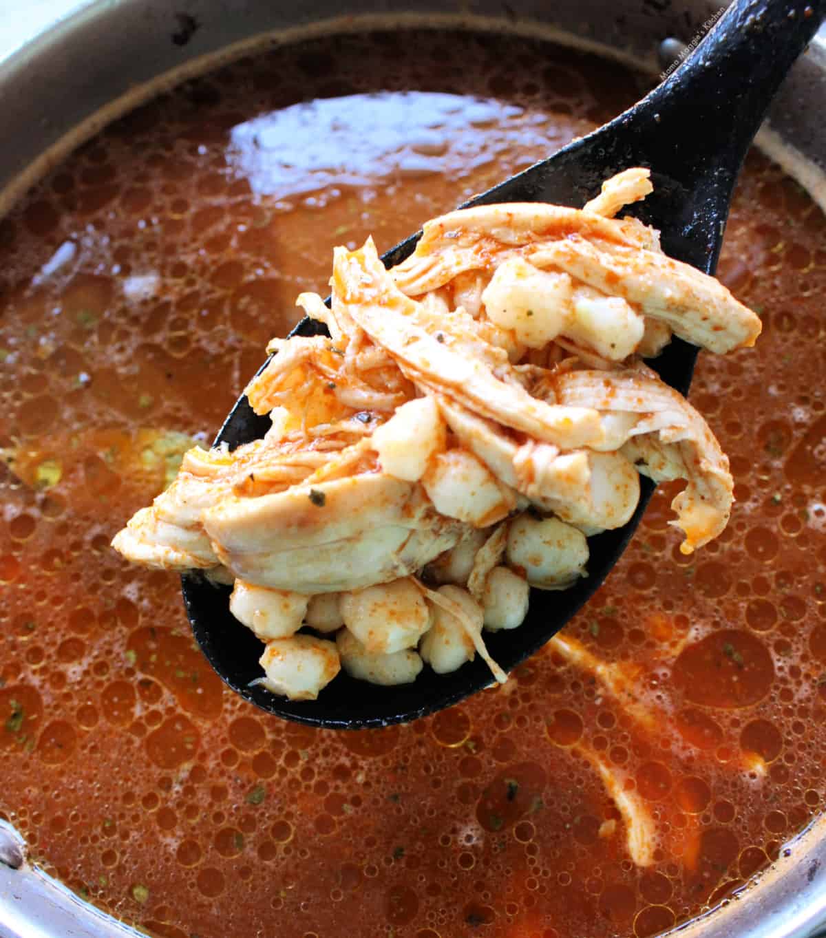 A spoon holding the chicken pozole over a stock pot.