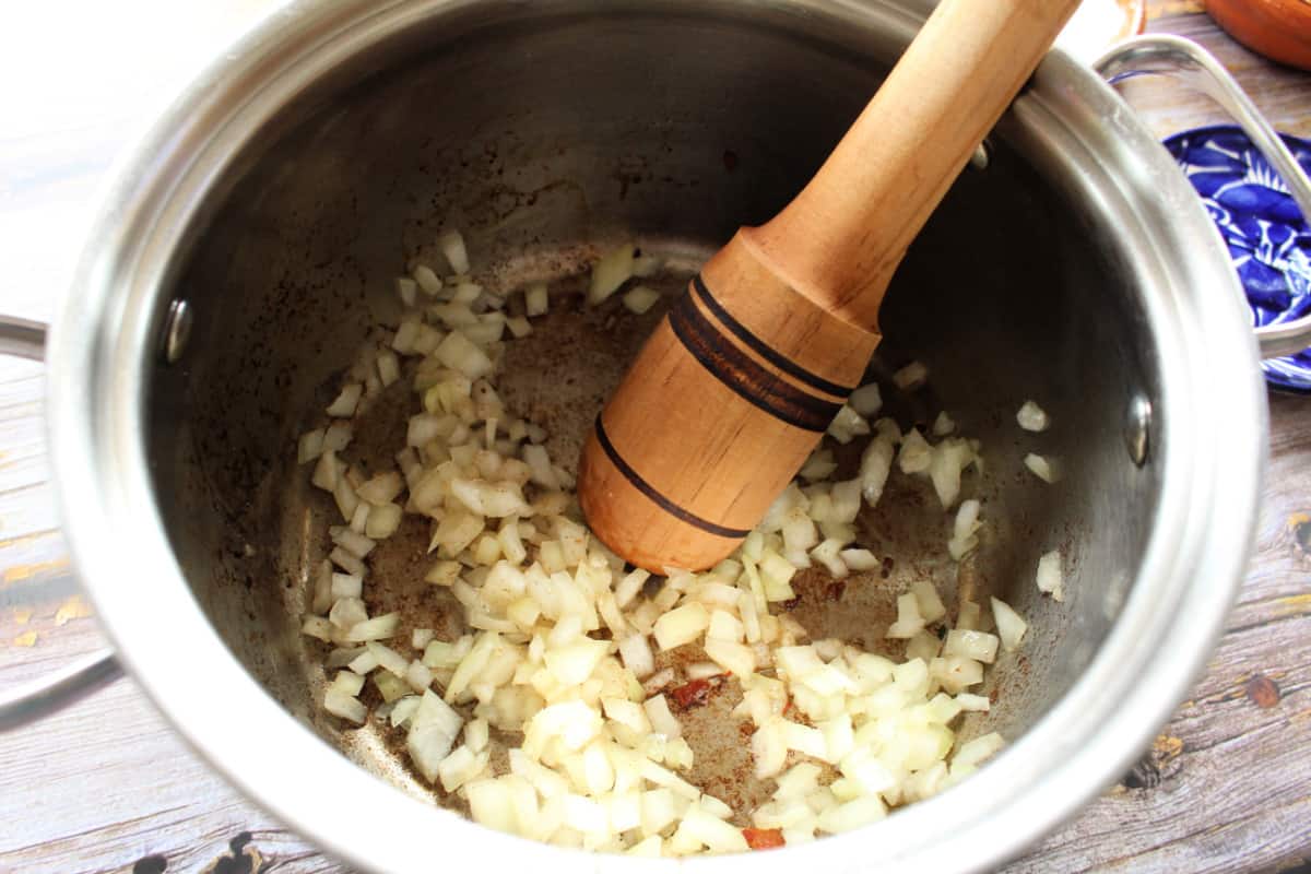 A wooden spoon inside a stock pot cooking diced onion.