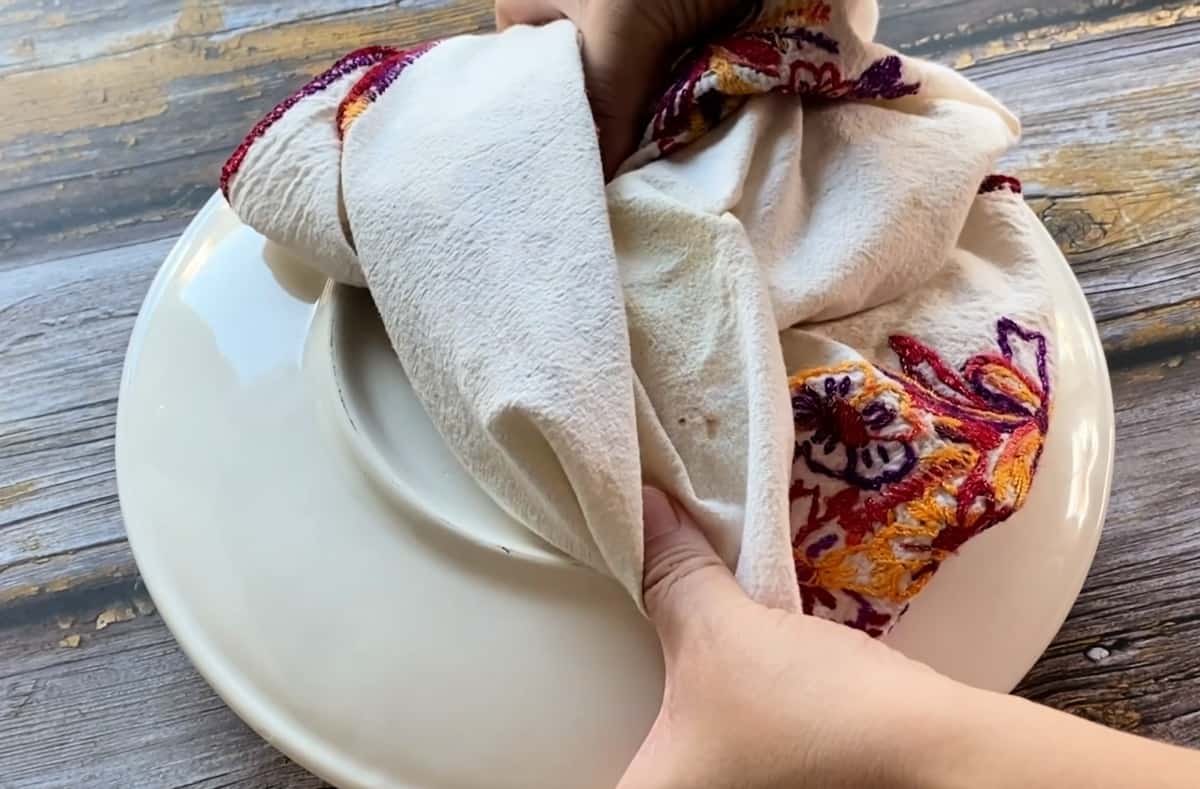 Two hands holding the edges of a large plate with a kitchen towel.