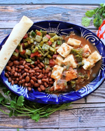Queso con Chile served in a decorative blue plate next to pinto beans and a cactus salad.