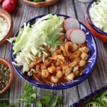 Red Chicken Pozole served in a decorative blue plate and surrounded by the toppings.
