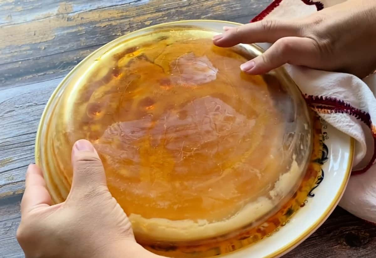 Two hands holding an upside down glass pie plate, molding the flan.