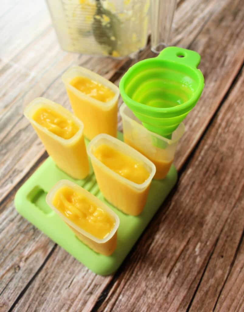 A green funnel on top of half full popsicle mold surrounded by other molds that are already filled.