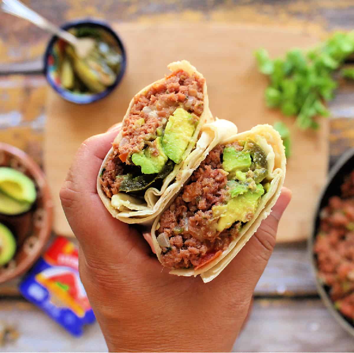 Hand holding two burritos showing the filling.