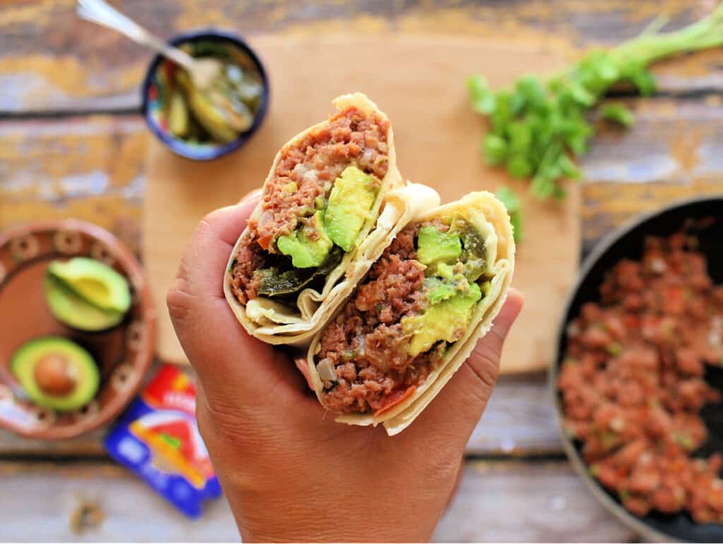A hand holding two burritos, exposing the filling.