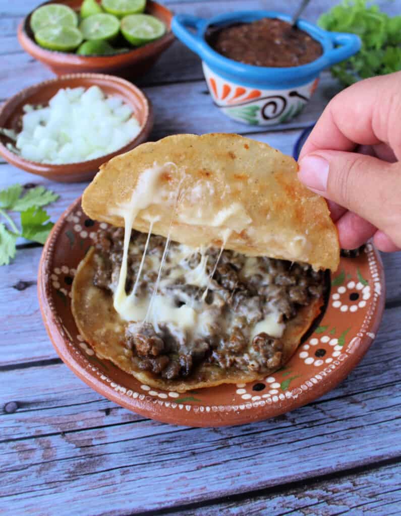 A hand pulling up the top tortilla showing the melted cheese inside mulitas.