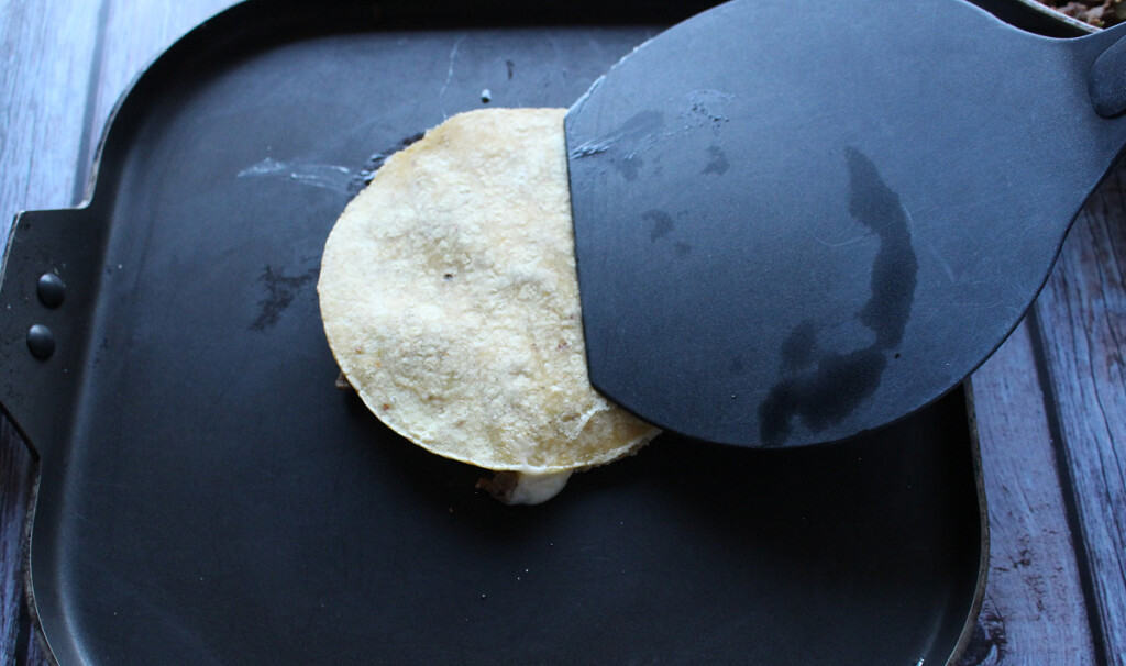 A black spatula pressing down on mulita that is cooking on a skillet.