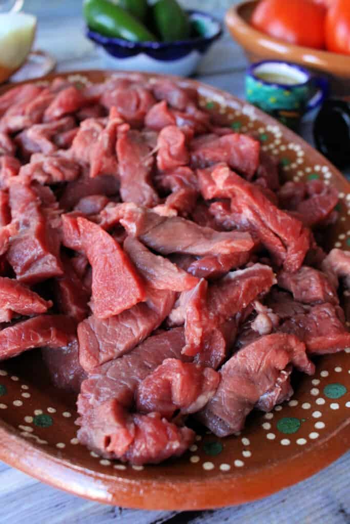 Raw beef strips on a decorative Mexican clay plate.