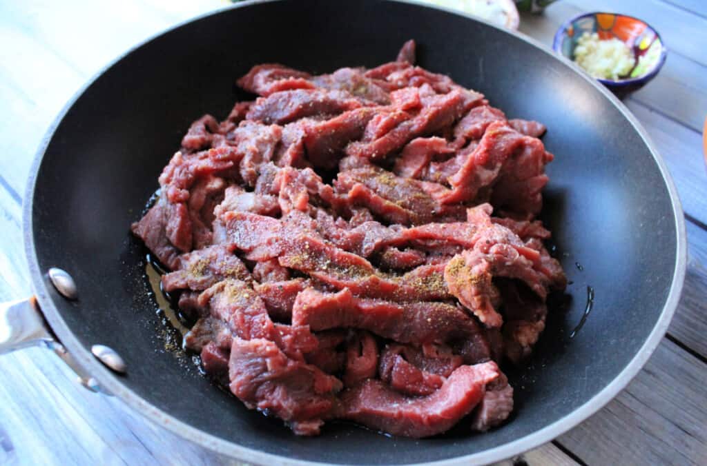 Raw beef strips cooking in a skillet.