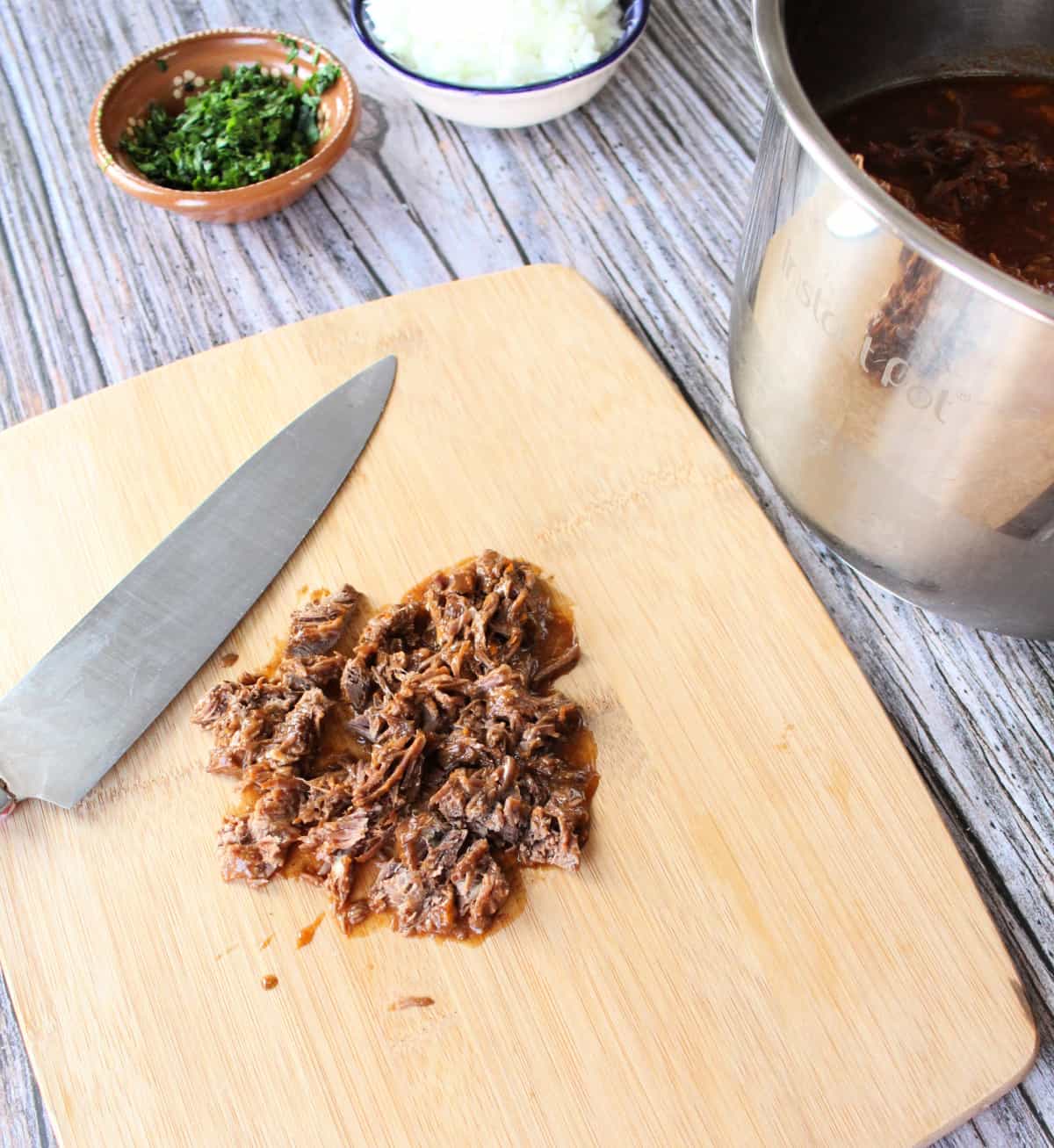 Chopped birria on a wooden cutting board next to a knife.