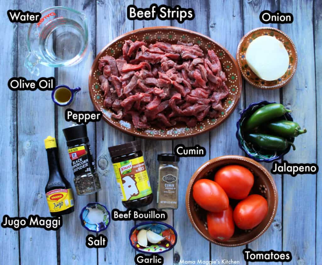 The ingredients needed to make Bistec a la Mexicana labeled and spread out on a wooden surface.