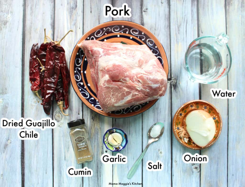 The ingredients necessary to make the slow cooker guajillo pork tacos labeled and spread out on a wooden table.