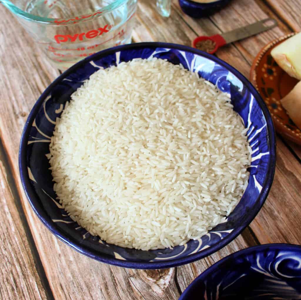 Long grain white rice in a blue bowl surrounded by other ingredients.