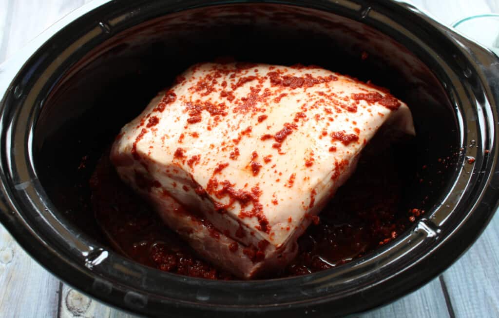 Raw pork covered in guajillo sauce in a slow cooker.