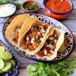 Slow cooker guajillo pork tacos served on a decorative plate next to the toppings.