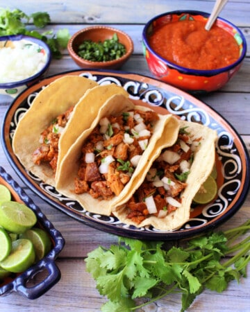 Slow cooker guajillo pork tacos served on a decorative plate next to the toppings.
