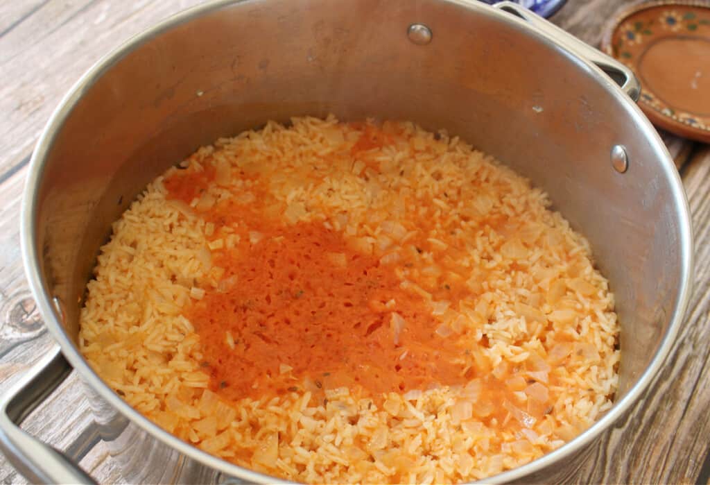 Mexican rice cooking in a stock pot with tomato sauce on top.