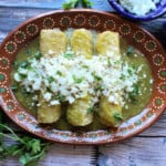 Enchiladas Verdes served on a decorative clay plate and topped with cheese and cilantro.