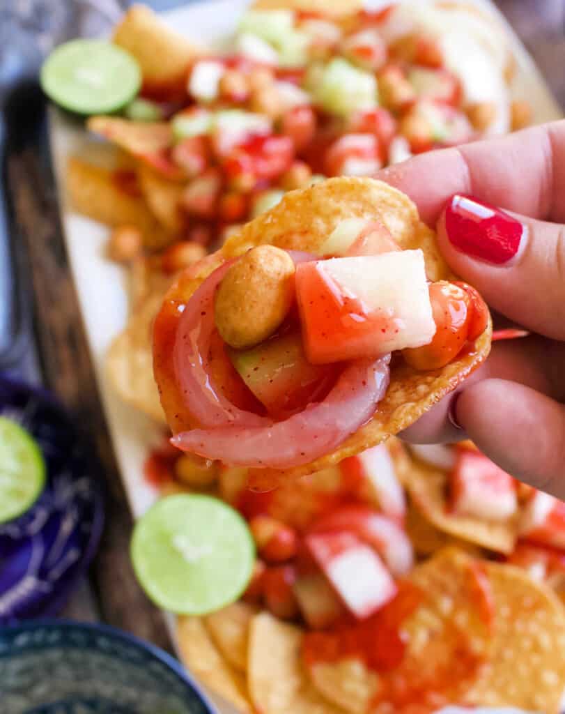 A hand holding a Tostilocos over a plate.