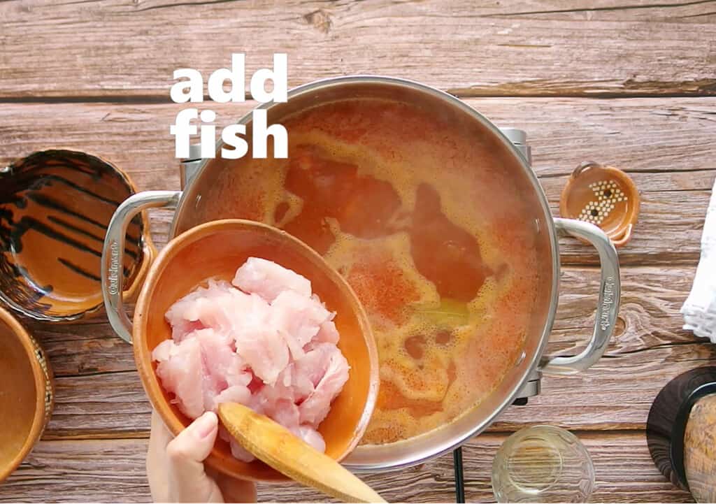 A picture of fish being added to a pot of tomato sauce.