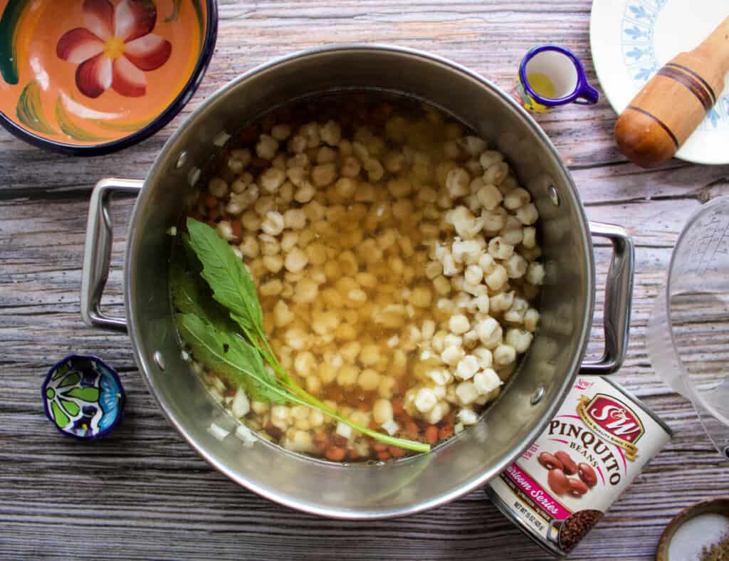 A pot of pozole cooking with a few epazote leaves.